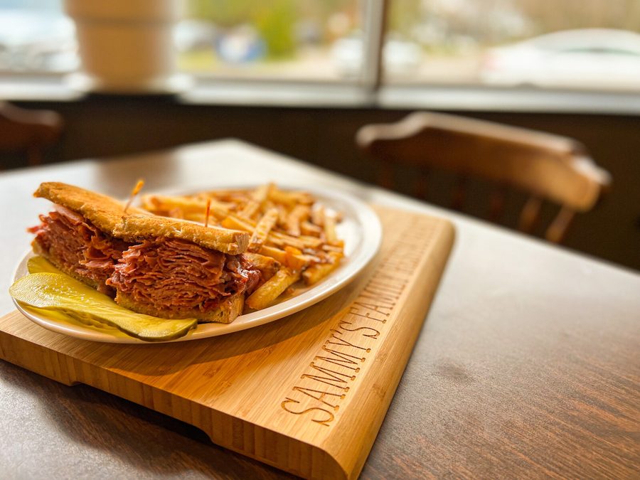 Corned beef on rye with fries and pickles on a Sammy's board by the window